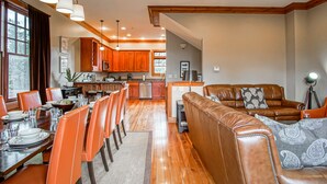 Amplia sala de estar con mesa de comedor, sillas color naranja, un sofá de cuero marrón y piso de madera.