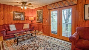 Un salon chaleureux avec des murs en bois, un ventilateur de plafond, un canapé rouge, une table basse et un tapis à motifs.