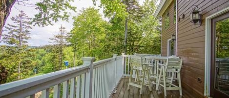 A wooden deck with white railings and outdoor furniture, overlooking a forested area.