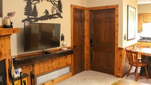 A kitchen with wooden cabinets, a built-in stove, a large flat-screen TV, and a decorative wall piece. - Whistlepunk 45- Modern Comfort With Mountain Charm-1 Bedroom (Snowshoe)