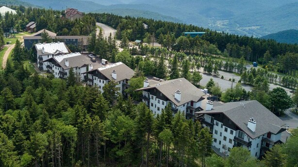 A resort with multiple buildings surrounded by dense forest and mountains in the background. - Whistlepunk 45- Modern Comfort With Mountain Charm-1 Bedroom (Snowshoe)