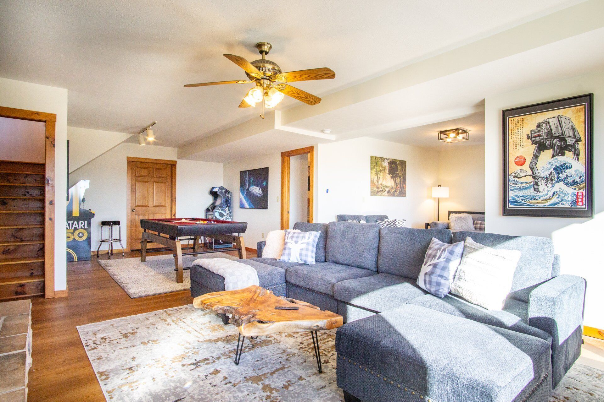 A living room with a sofa, coffee table, and a ceiling fan. There is a pool table and a door leading to another room.