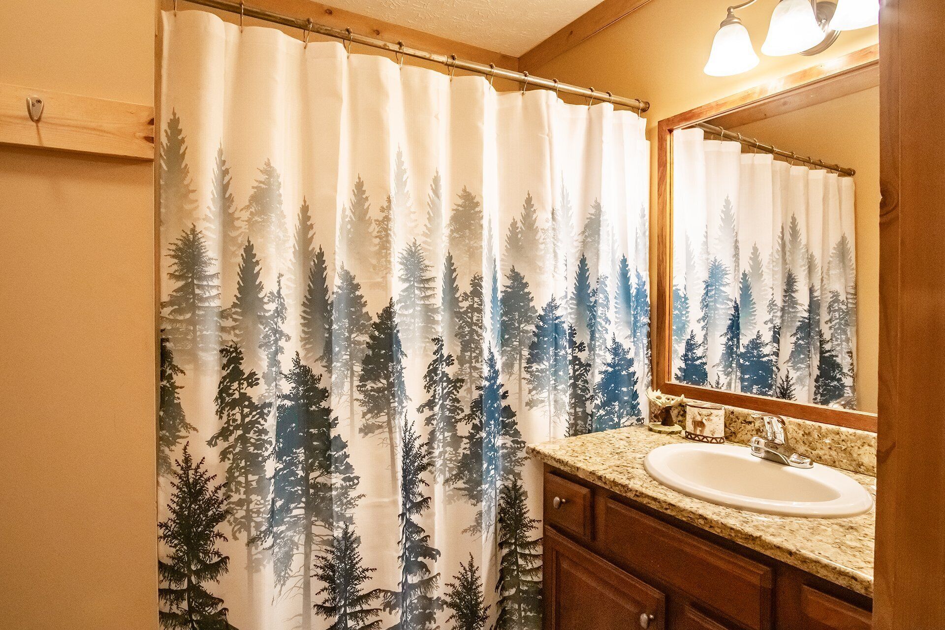 Een badkamer met douchegordijn met een natuurprint, een wastafel en een houten opbergmeubel.