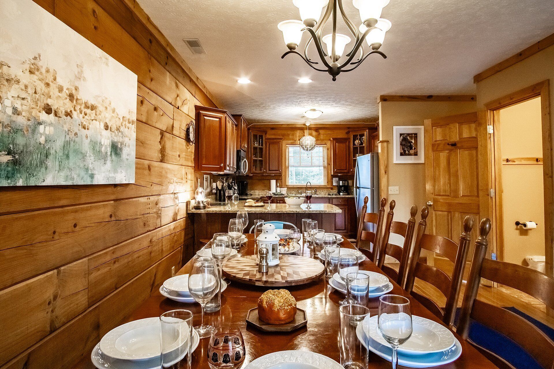 A wooden interior with a dining table set for six, a chandelier, and wooden cabinets.