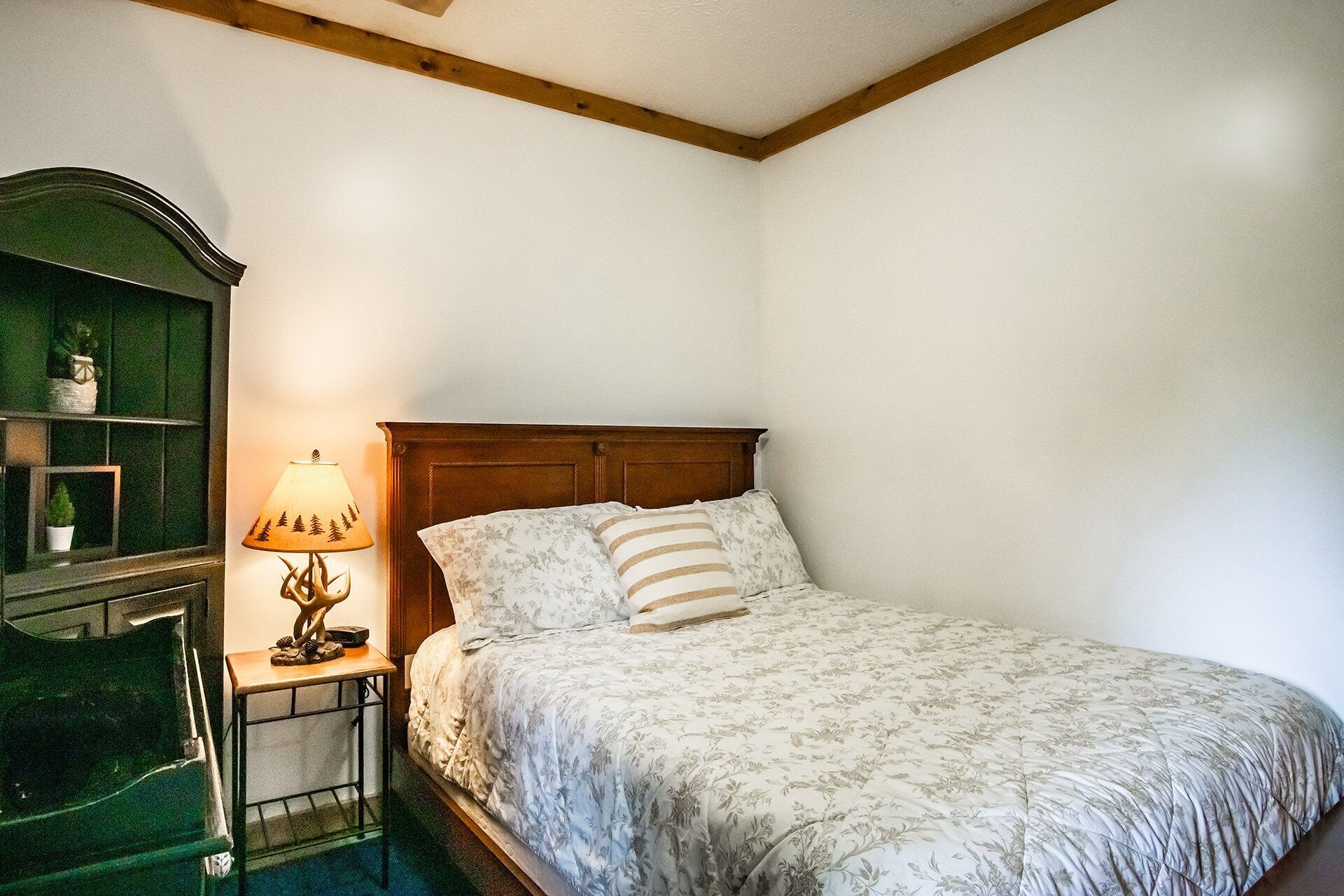 Un dormitorio con una cama de madera, una mesita de noche con lámpara y un armario verde.