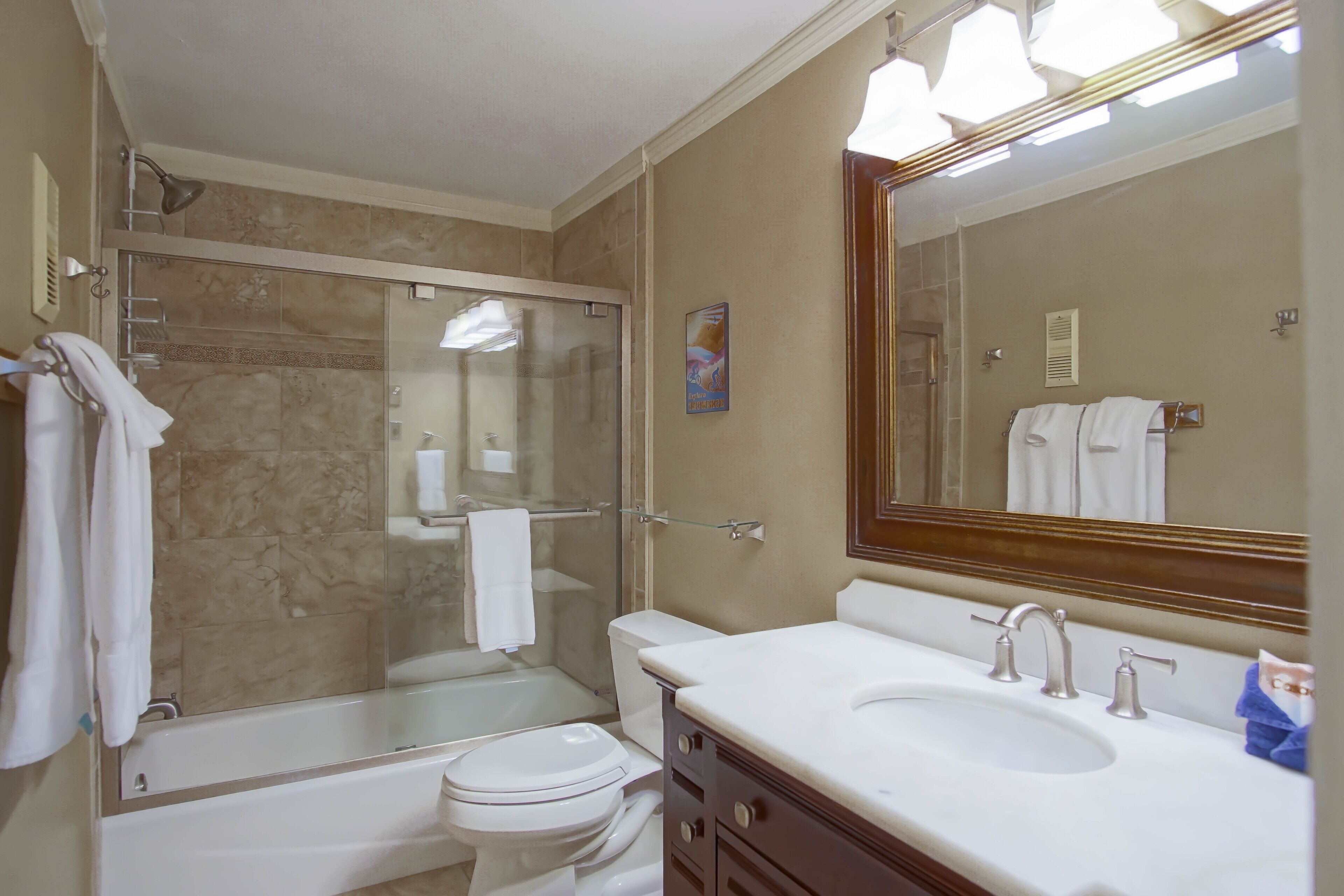 Une salle de bain avec une douche à parois de verre, des toilettes, un lavabo avec un miroir et des serviettes suspendues sur un porte-serviettes.