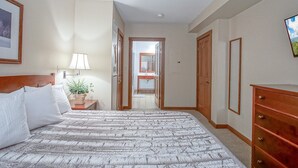 Habitación de hotel con cama, mesita de noche con lámpara, cómoda y espejo en la pared.