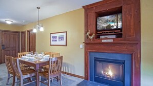 Un comedor con chimenea, sillas de madera, una mesa dispuesta para cuatro comensales y un cuadro en la pared.