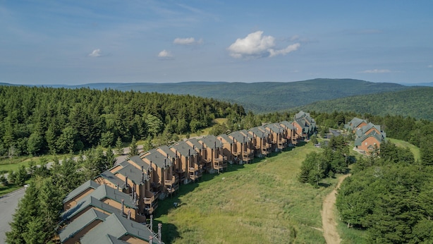 A row of log cabin-style buildings with a central walkway, surrounded by forested hills. - 1 Br: Powderidge 30:slope Side, Pet Friendly end Unit on Shuttle Route (Snowshoe)