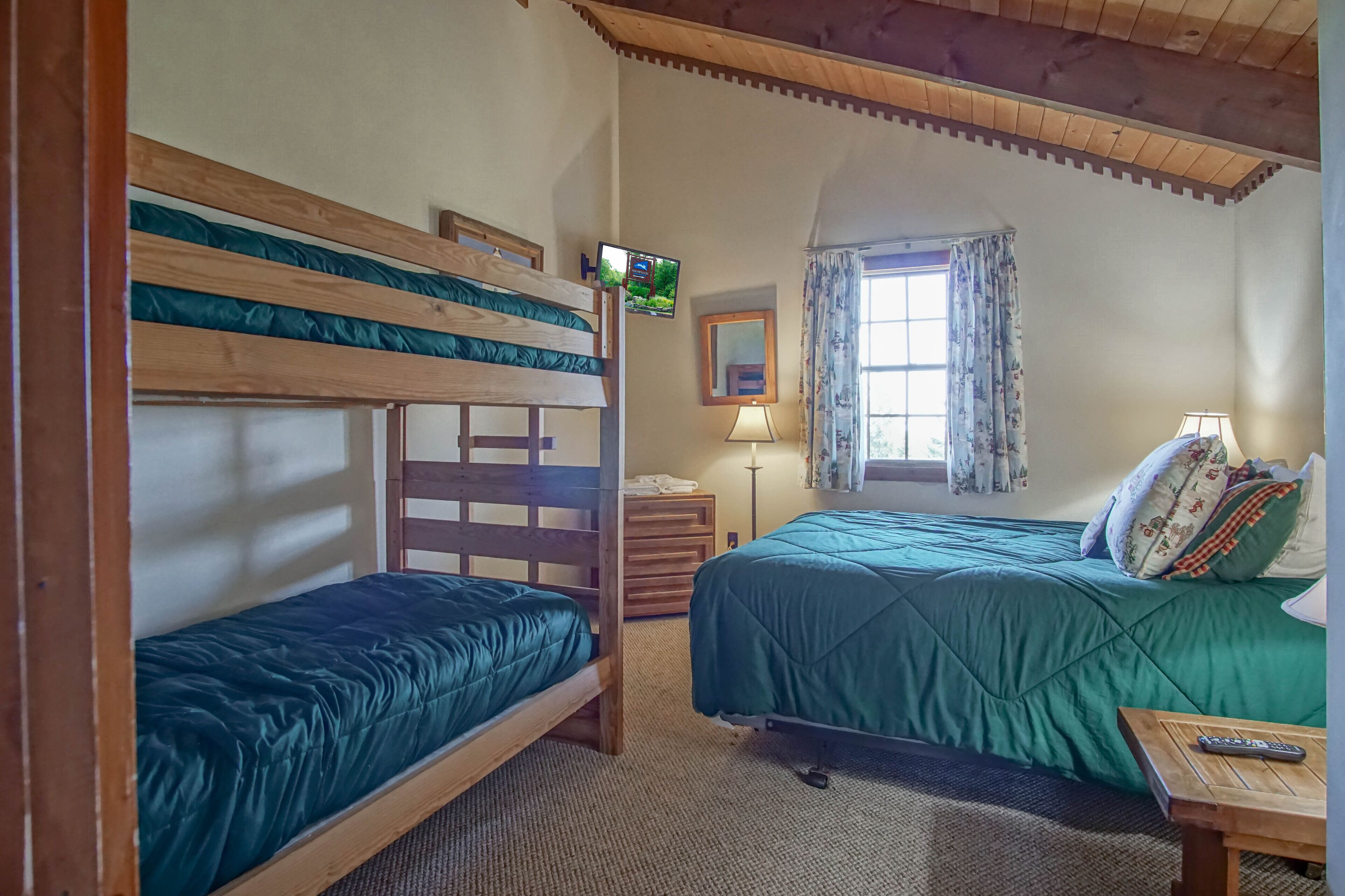 Ein Zimmer mit Etagenbetten, einem Fernseher, einer Lampe, einem Fenster mit Vorhängen und einem kleinen Tisch.