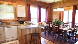 A wooden cabin-style kitchen with a central island, bar stools, and a dining table set for four. - 4 BR: Timbers #1 Stand Alone Cabin (Snowshoe)