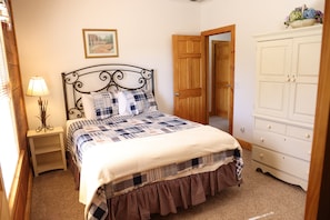 A bedroom with a bed, a nightstand, a lamp, a wooden door, and a white dresser. - 4 BR: Timbers #1 Stand Alone Cabin (Snowshoe)
