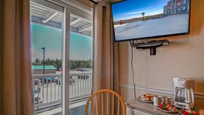 Habitación de hotel con balcón, televisor en la pared, mesa de comedor con platos de comida, cafetera y una silla.