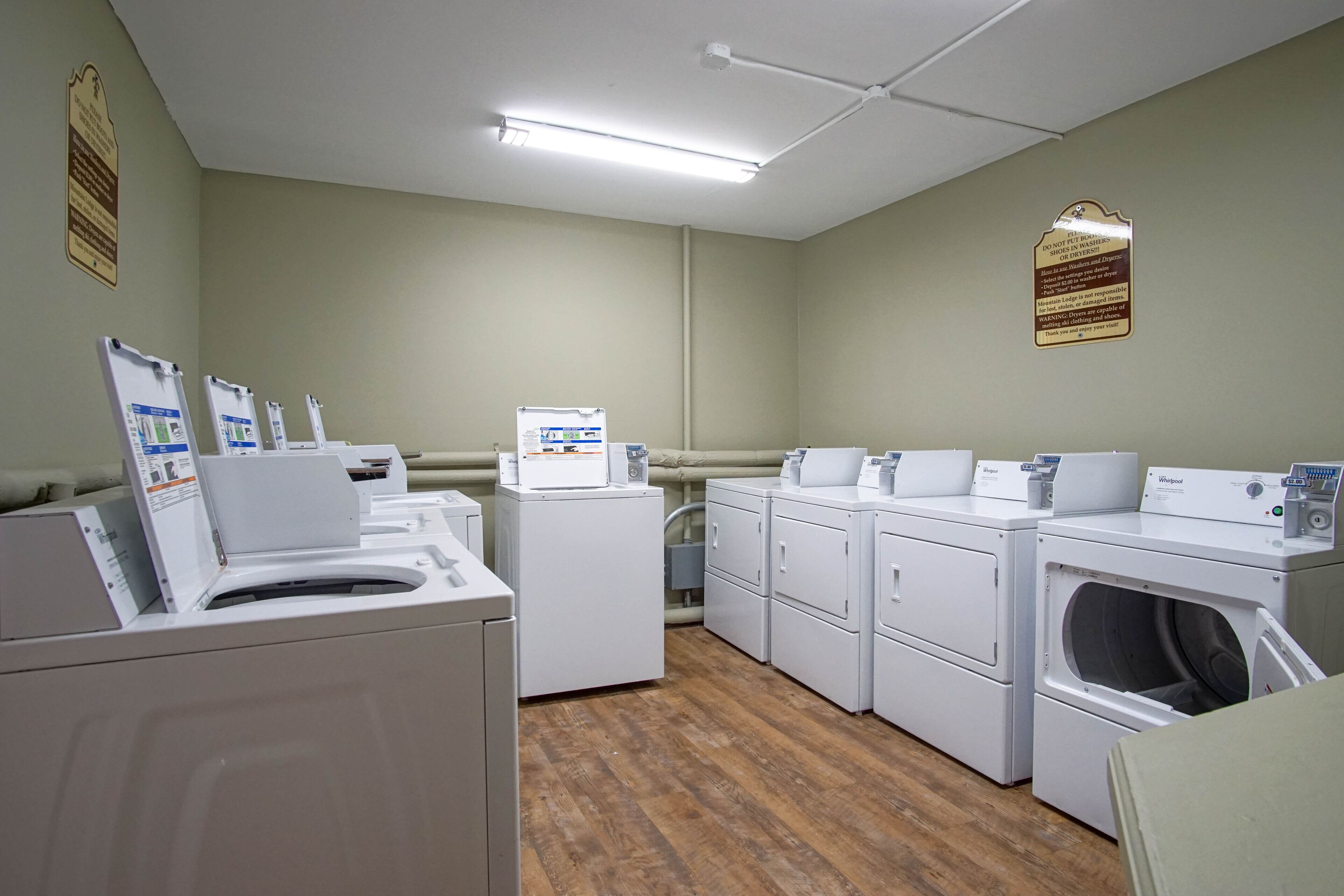 A laundry room with multiple washing machines and dryers, wooden flooring, and instructional signs on the walls.