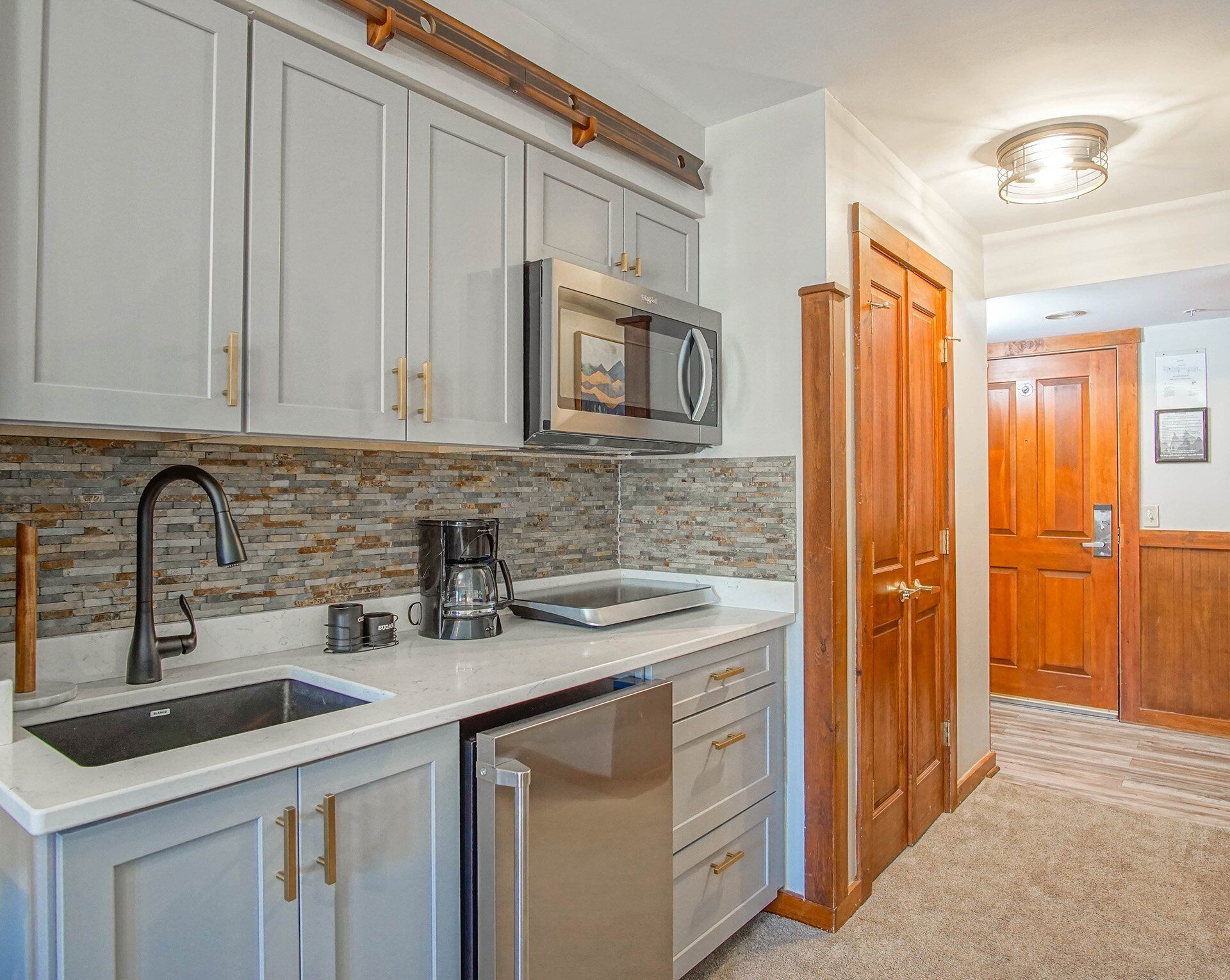 A kitchen with grey cabinets, a stainless steel sink, a coffee maker, and a microwave.