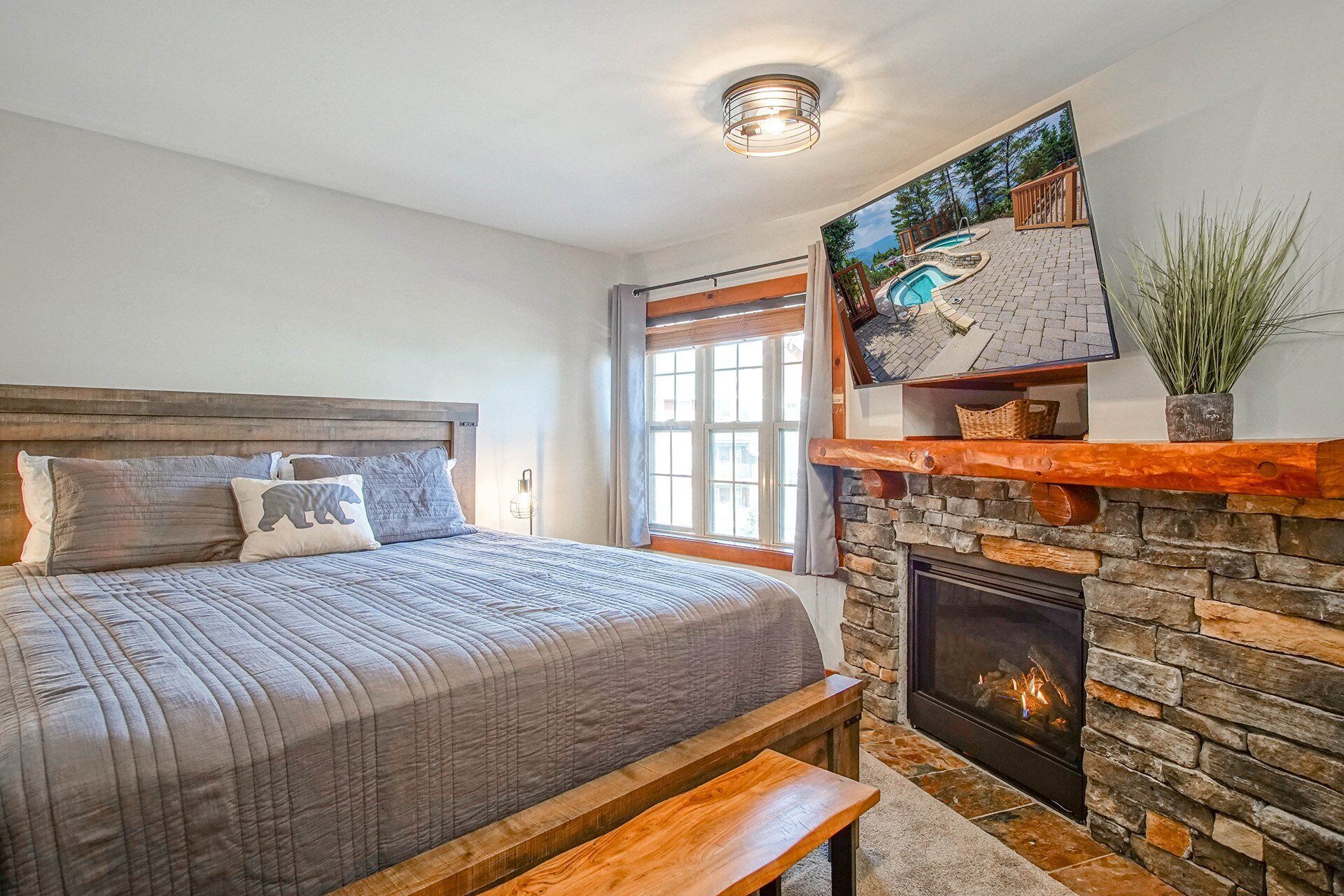Une chambre avec un grand lit, une cheminée en pierre et une vue sur une piscine, visible par la fenêtre.