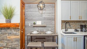 A compact kitchen with a stone wall, a wooden bench, a hanging light fixture, and a built-in shelf with a small plant and a framed picture. - Rimfire 421 Cozy Studio Just Steps From the Village Slope Side (Snowshoe)