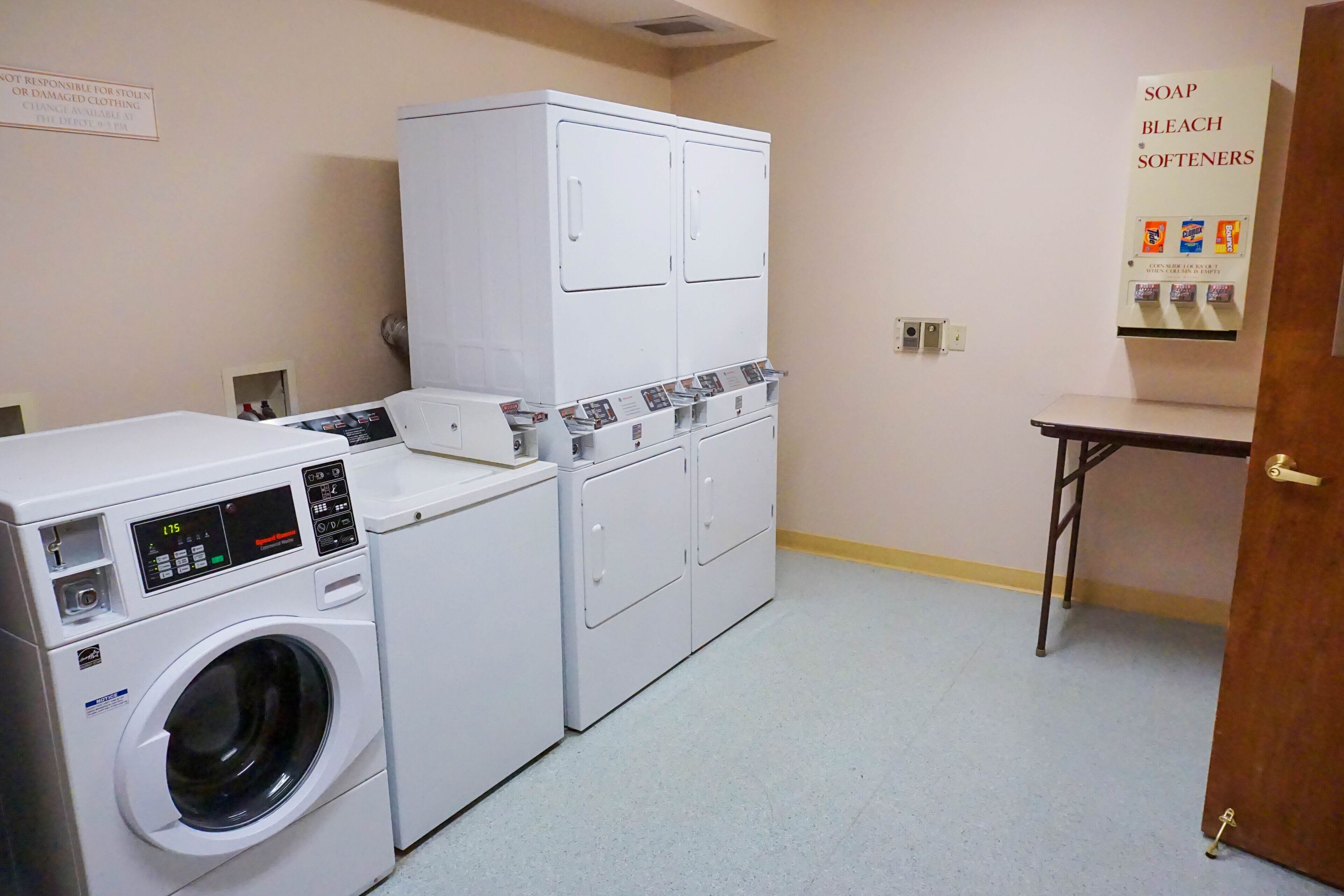 A laundry room with a front-loading washer and dryer, a cabinet with shelves, and a soap and bleach dispenser.