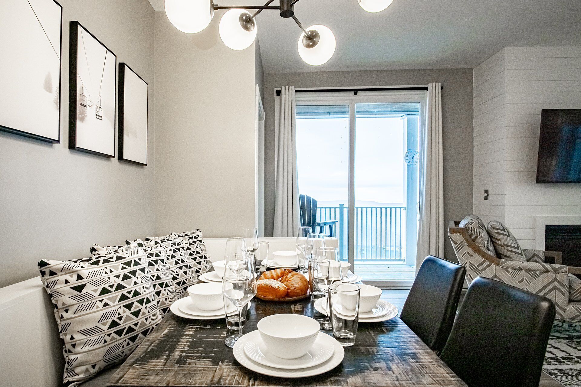 Un comedor con una mesa preparada para cuatro personas, un sofá con cojines estampados y vistas al exterior a través de un ventanal.