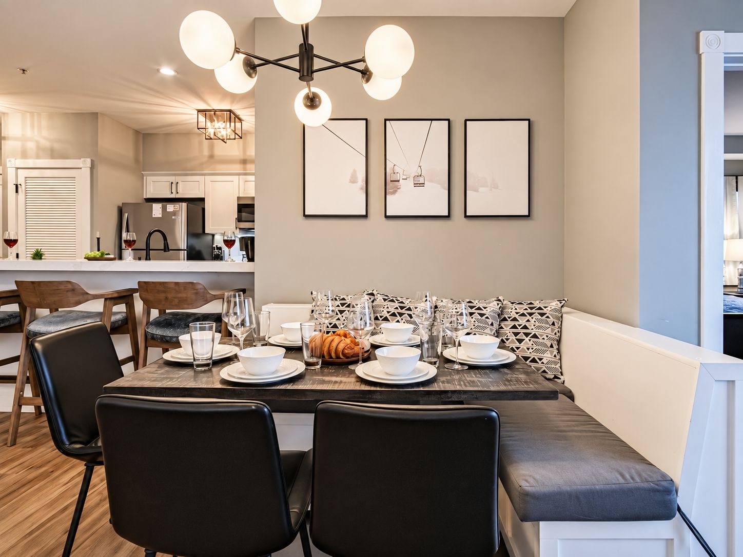 Un comedor con una mesa dispuesta para cuatro personas, sillas, un banco y una araña.