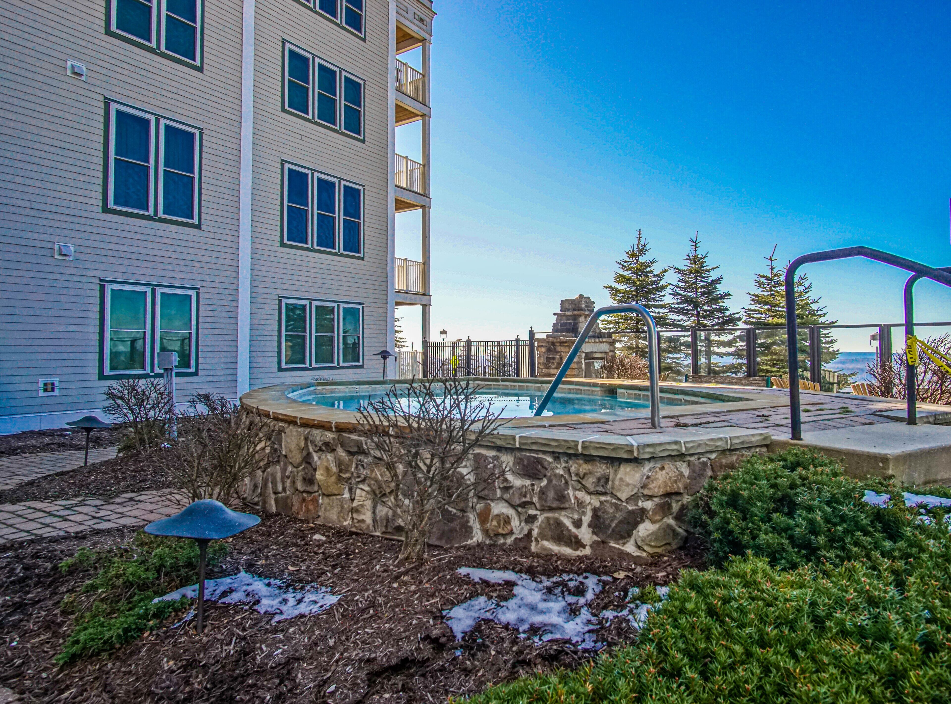 A residential building with a swimming pool, stone walls, and a view of trees and mountains.