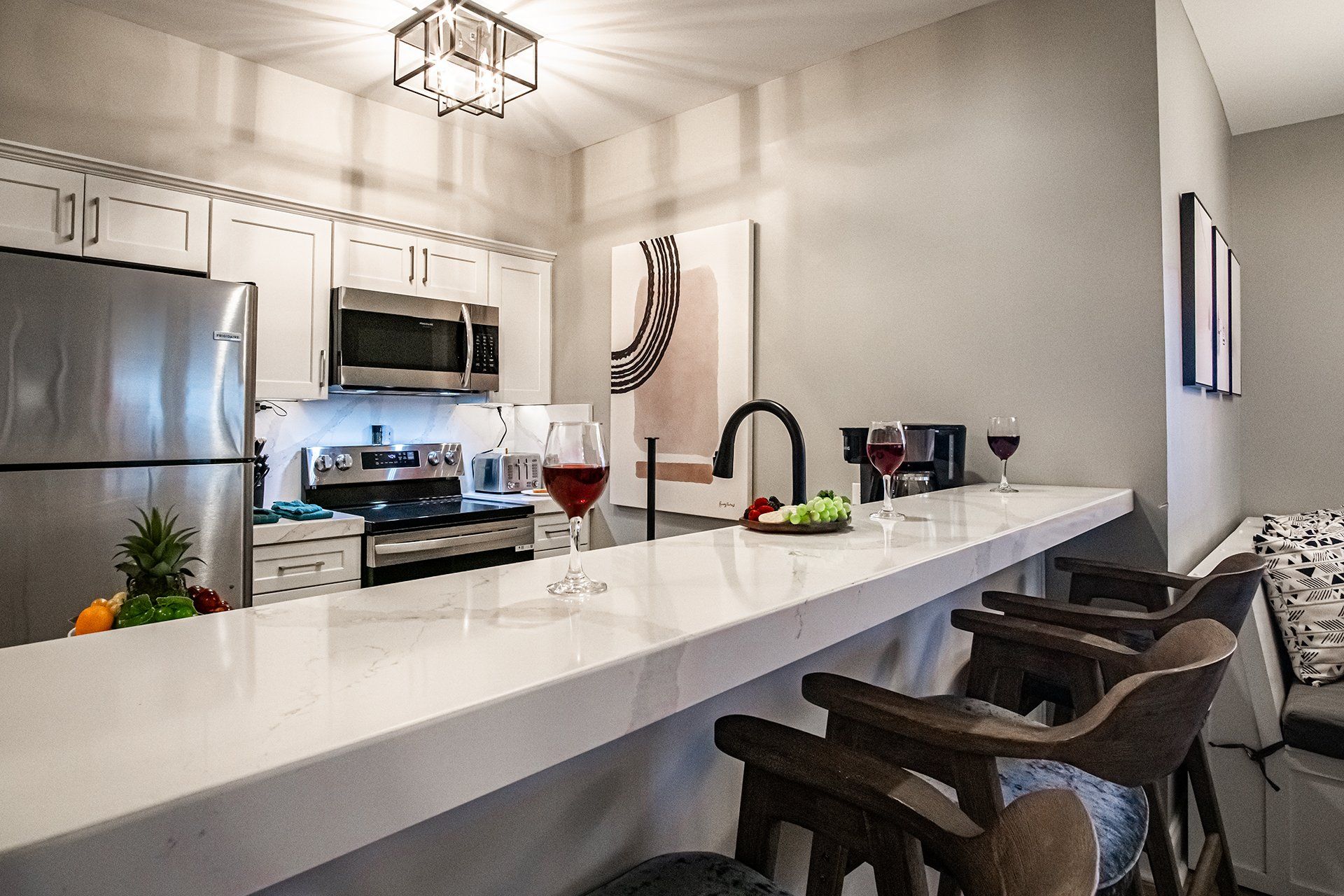 A modern kitchen with stainless steel appliances, a marble countertop, and a bar area with wooden chairs.