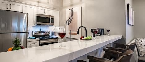 A modern kitchen with stainless steel appliances, a marble countertop, and a bar area with wooden chairs.