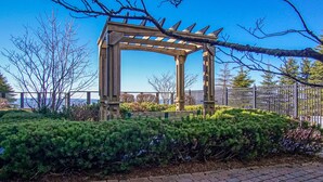 Une structure de pergola en bois, située dans un jardin aménagé, avec un chemin bordé de briques.