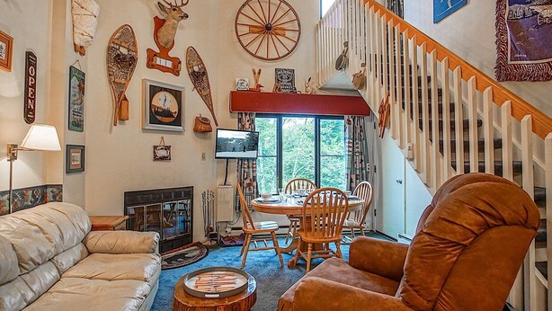 A cozy living room with a fireplace, a dining area with a wooden table and chairs, and a staircase with a white railing. - Silver Creek 5216 - The Winter`s Amazing 2 Br Condo (Snowshoe)