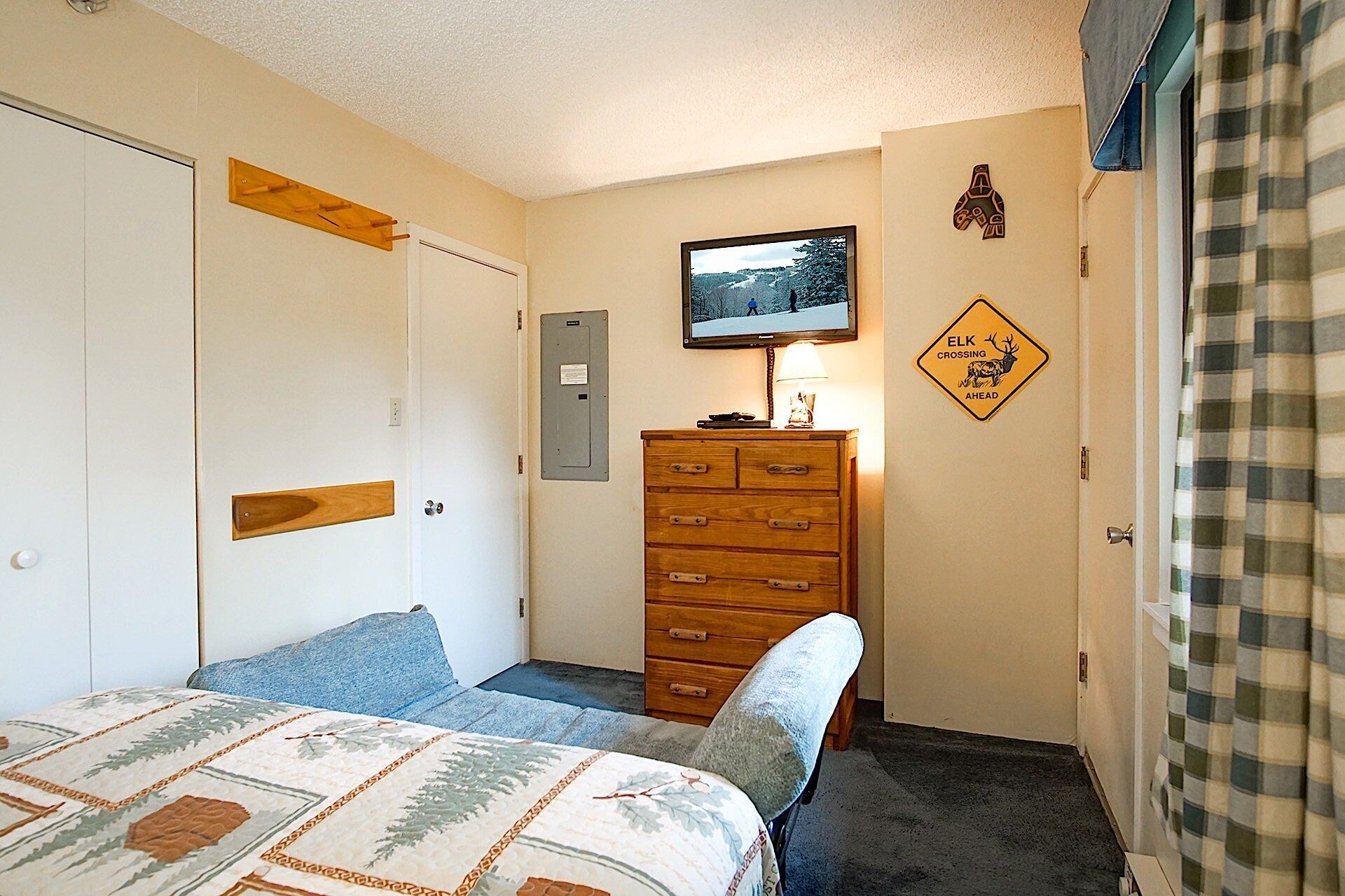 A bedroom with a bed, a dresser, a television on the wall, and a sign indicating an elk crossing ahead.