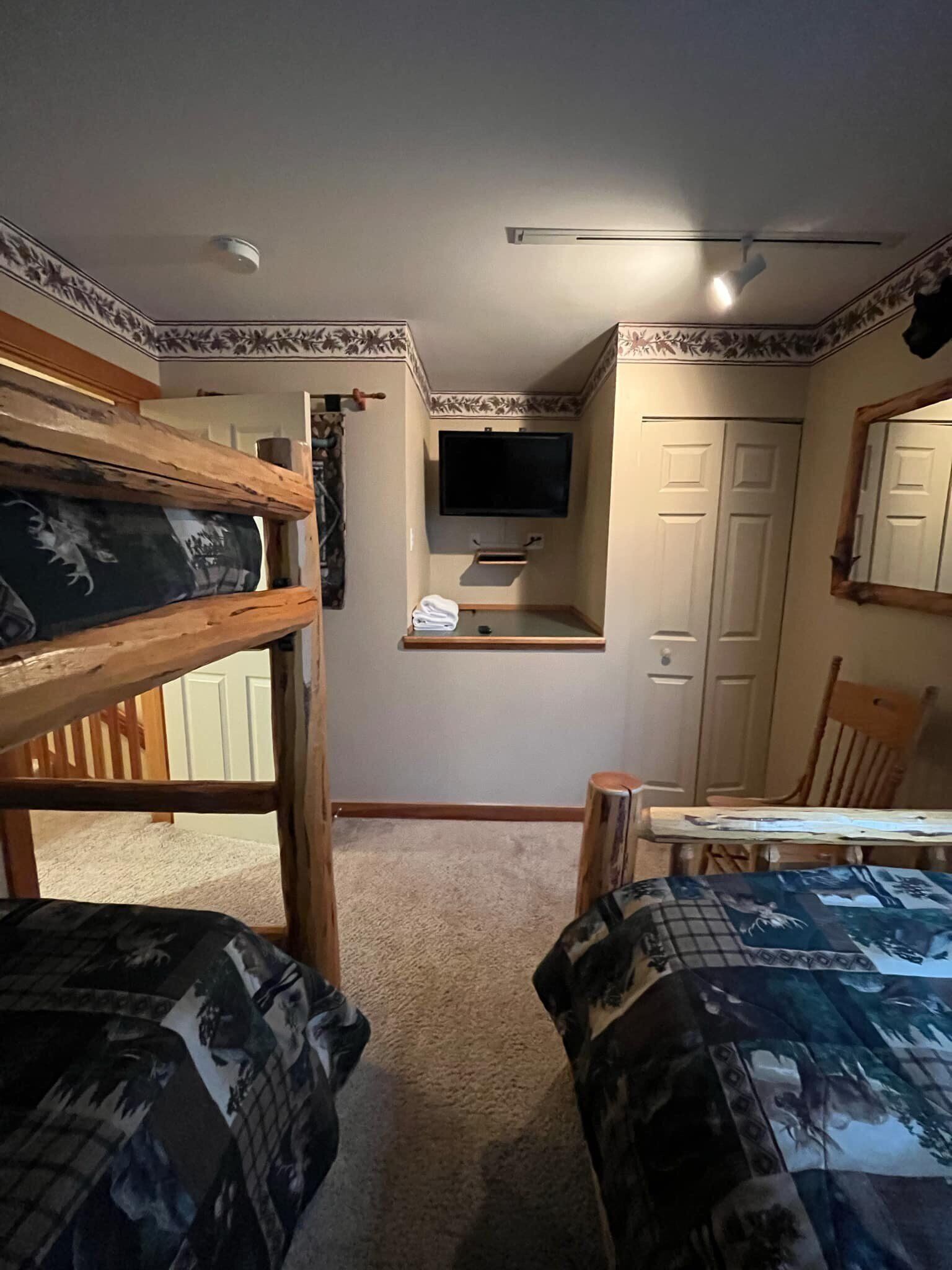 A room with bunk beds, a small desk with a television, and a mirror on the wall.