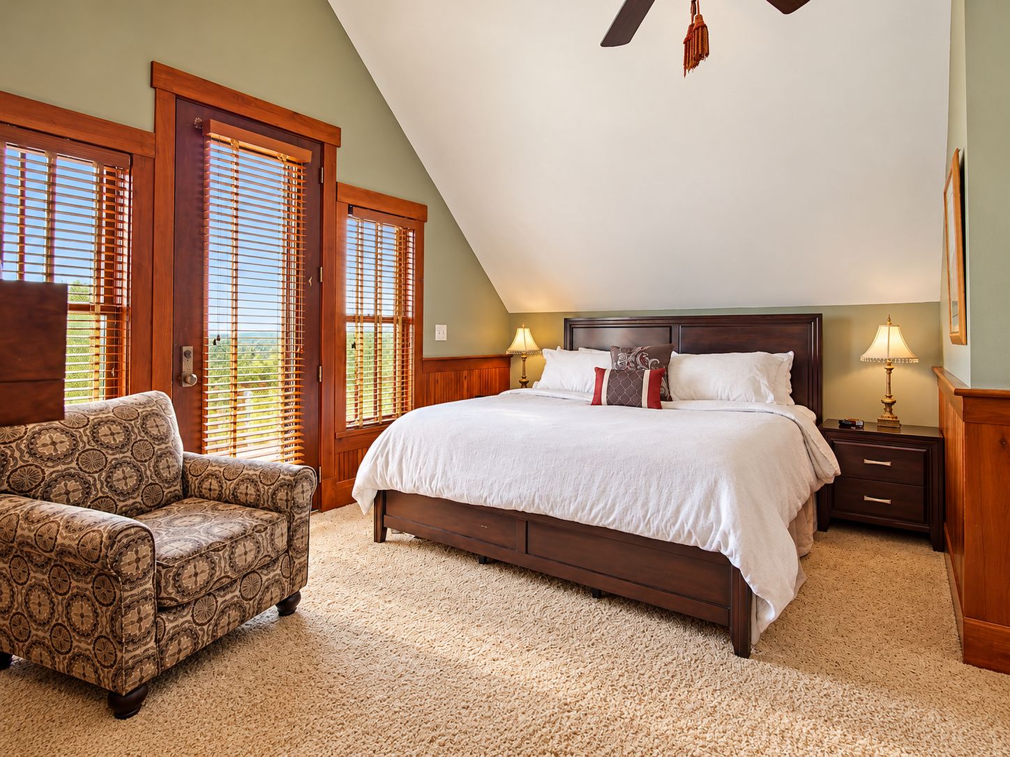 A bedroom with a large bed, two bedside tables, a chair, and a ceiling fan.