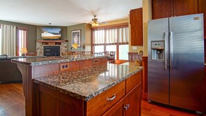 A kitchen with a granite countertop, wooden cabinets, a stainless steel refrigerator, and a built-in island with seating.