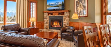 A living room with a stone fireplace, leather furniture, a television, and a large window with a mountain view.