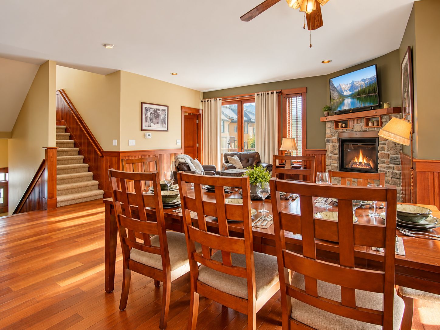 A dining area with wooden chairs and a table, a fireplace, and a television mounted on the wall.
