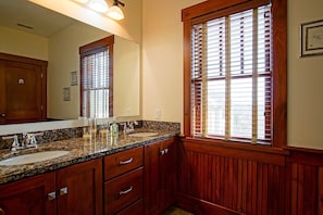 A bathroom with wooden paneling, a granite countertop, a sink, and a window with blinds.