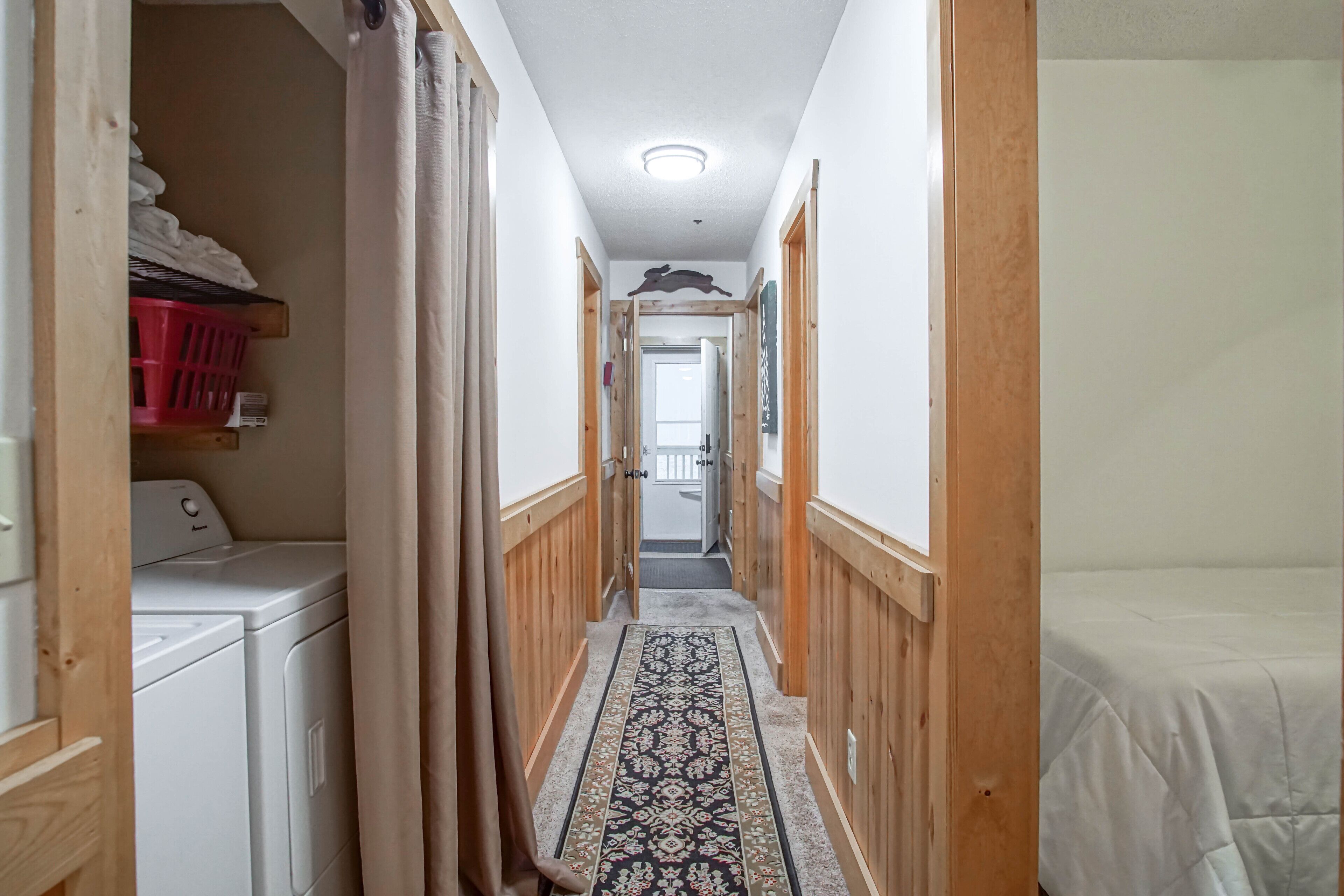 A narrow hallway with a patterned rug, wooden walls, and a washing machine on the left.