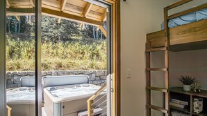 A modern outdoor hot tub area with a stone wall backdrop, a wooden pergola, and a built-in bookshelf with various items. - 3 Bedroom: Coal Box Beautiful Unique Home Close to Slopes (Snowshoe)