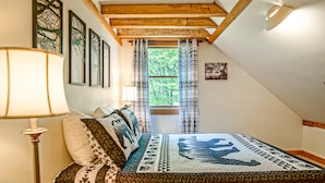 Ein gemütliches Schlafzimmer mit karierter Bettdecke, einem Holzkopfteil und einem Fenster mit gemusterten Vorhängen.