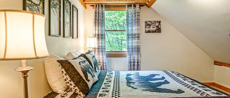 A cozy bedroom with a checkered bedspread, a wooden headboard, and a window with patterned curtains.
