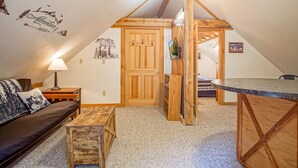 Ein gemütliches Schlafzimmer unter dem Dach mit Holzbalkendecke, einem Bett, einem Schreibtisch und einem an der Wand montierten Fernseher.