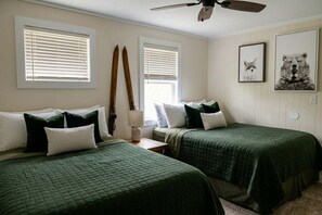 Ein Zimmer mit zwei Betten, einem Deckenventilator und zwei Fenstern mit Jalousien.