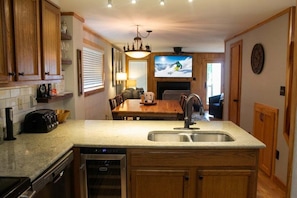 A kitchen with a built-in dishwasher, a dining area with a wooden table and chairs, and a large flat-screen TV mounted on the wall. - Powderidge 15 Slope Side (Snowshoe)