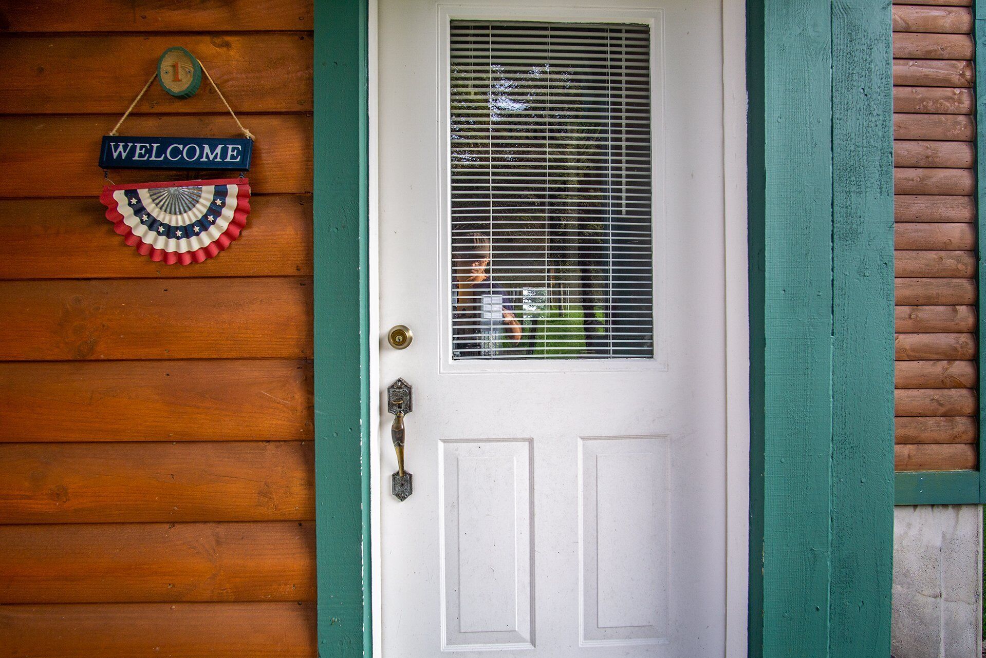 A white door with a green trim, a window with blinds, and a 'WELCOME' sign with a red, white, and blue ribbon.