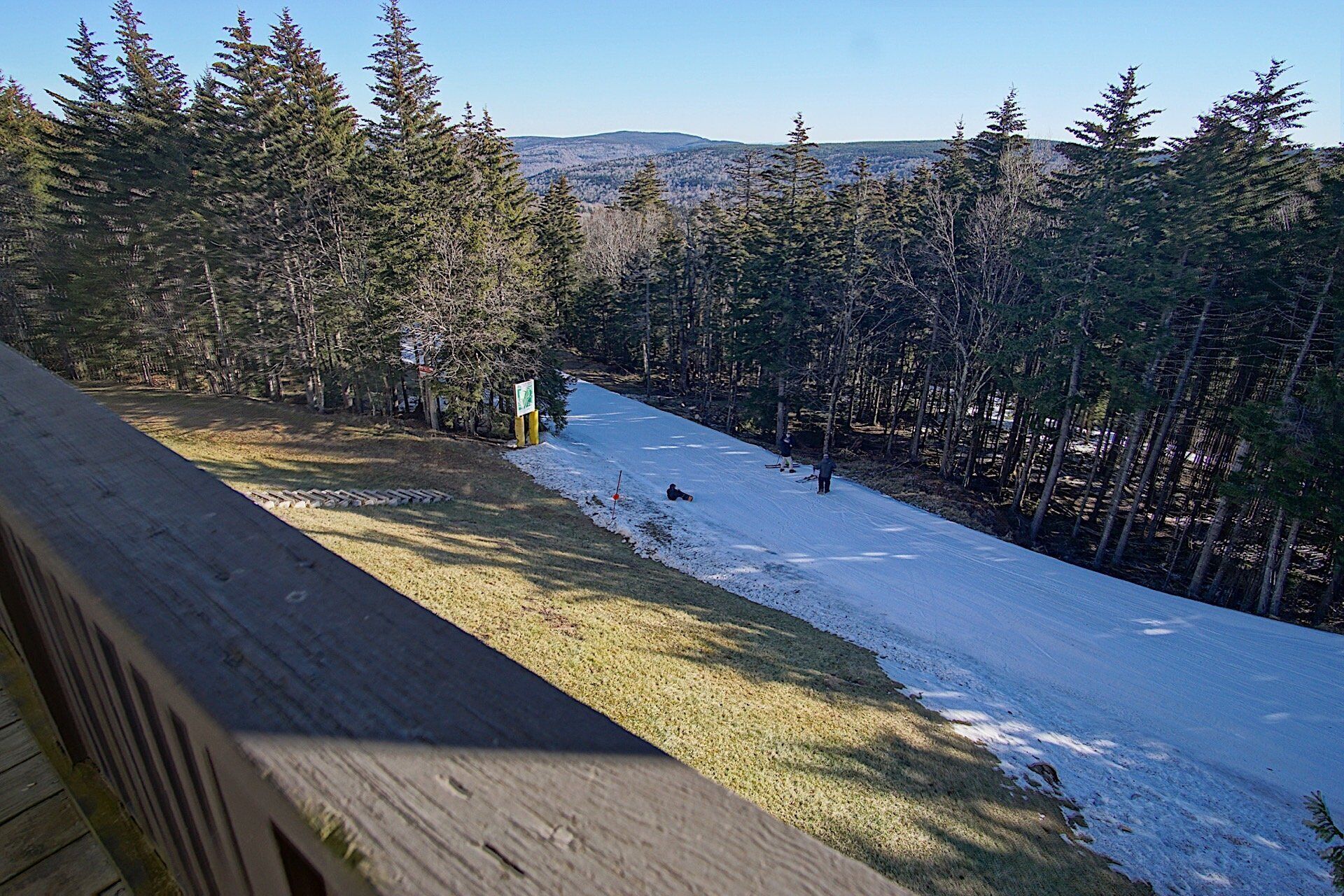 Une piste de ski enneigée, avec une plateforme d’observation en bois et un panneau indicateur.