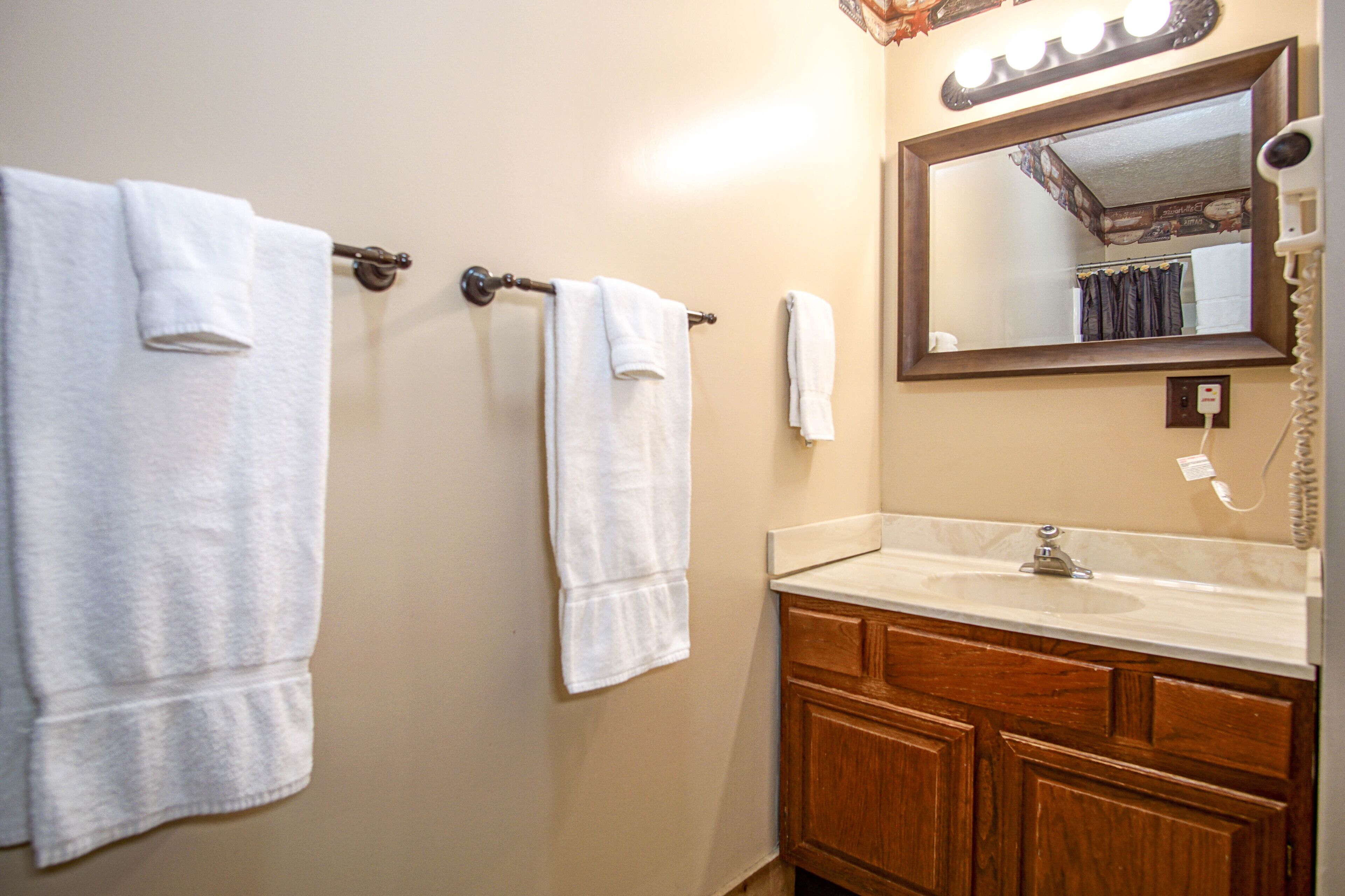 A bathroom with two towels hanging on a towel rack, a sink, and a mirror with lights above it.