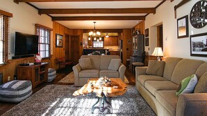 A cozy living room with a fireplace, a television, and a dining area with wooden cabinets and a kitchen in the background. - Whistlepunk 20 Wilderness Hideaway, Slope Side, Spacious 2 Br Condo (Snowshoe)