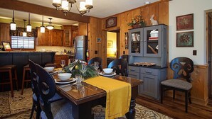 A dining area with a wooden table, chairs, and a chandelier. There is a kitchen in the background with wooden cabinets and a refrigerator. - Whistlepunk 20 Wilderness Hideaway, Slope Side, Spacious 2 Br Condo (Snowshoe)