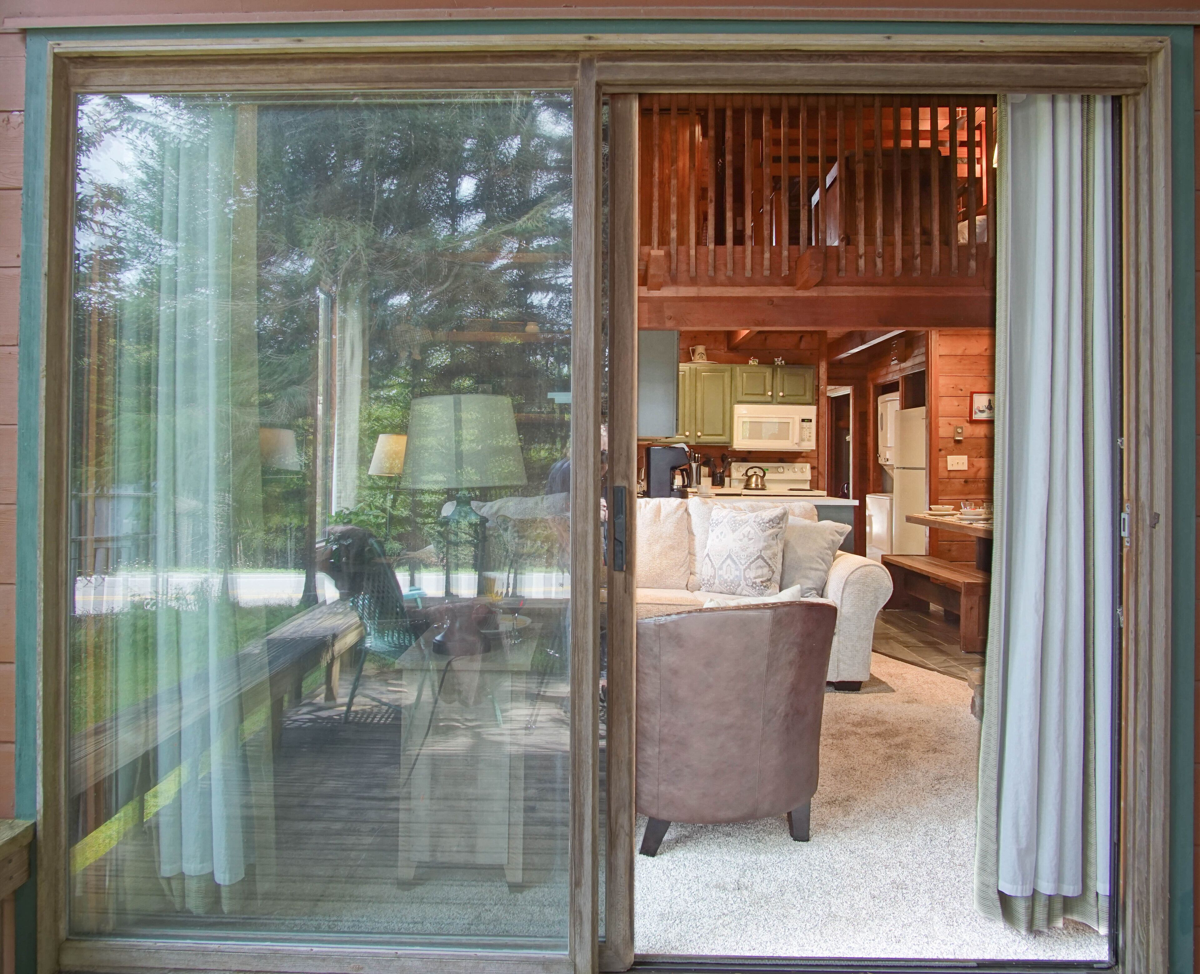 A cozy interior with a sliding glass door leading to a living area featuring a sofa, a coffee table, and a kitchen area with a microwave and stove.