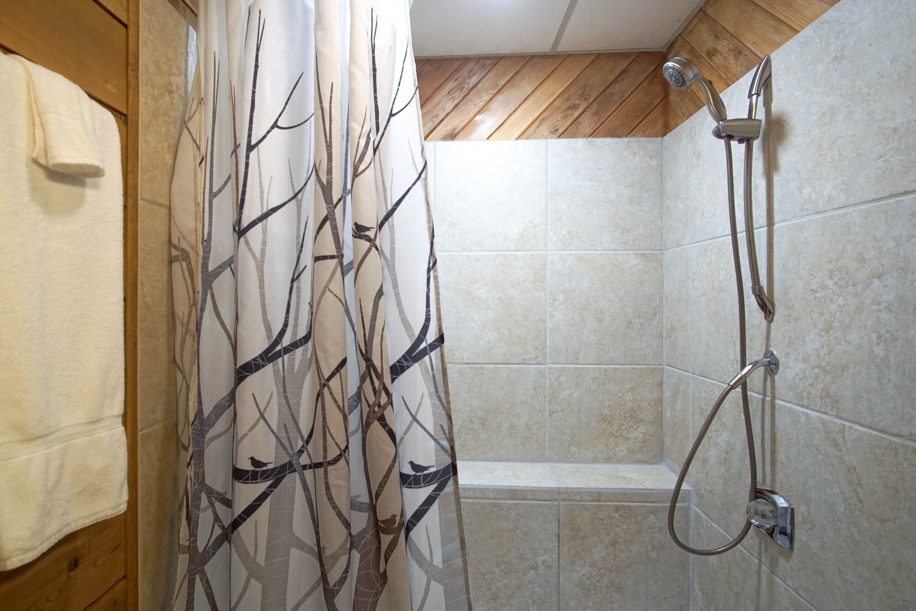 A shower area with a tree-patterned shower curtain, a handheld showerhead, and a towel rack.
